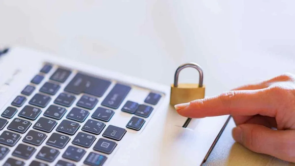 Dedo tocando um cadeado dourado sobre o teclado de um notebook
