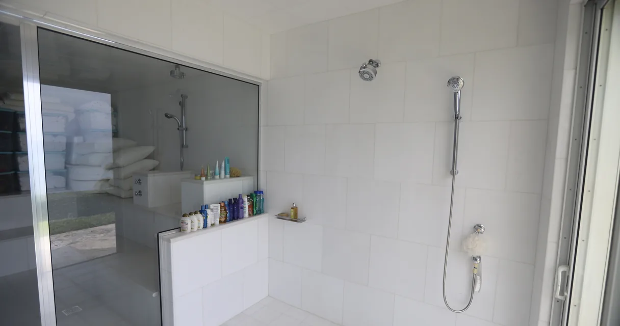 Box de vidro com ducha em um banheiro de azulejos brancos, ilustrando como limpar vidro de box do banheiro